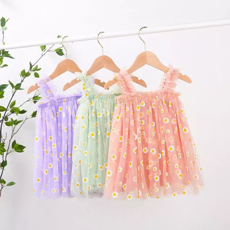 There are 3 dresses hanging up. One is purple with white and yellow daisies, another is green with white and yellow daisies and the last one is pink with white and yellow daisies.